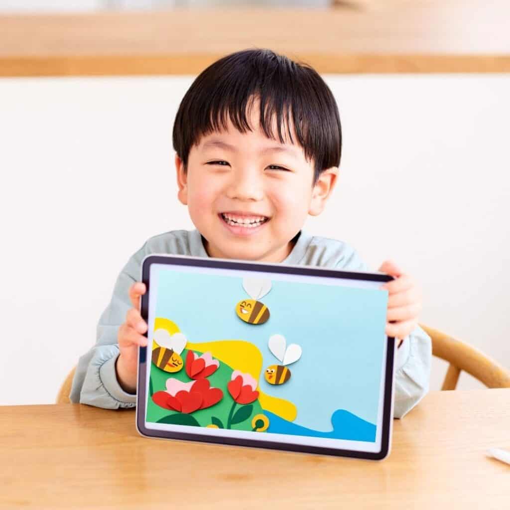 Smiling child holding a tablet displaying a colorful digital artwork of bees and flowers
