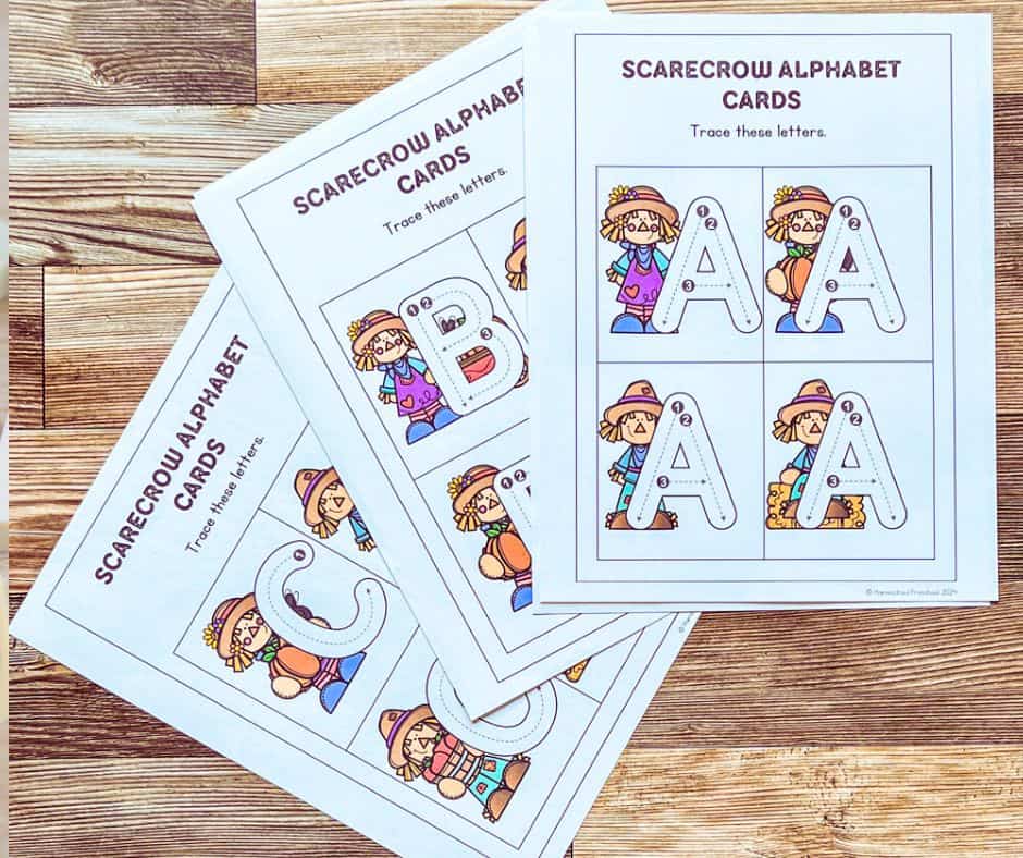 Three scarecrow-themed alphabet tracing sheets with letters A, B, and C are placed on a wooden surface. Each sheet shows uppercase and lowercase letters with scarecrow illustrations.